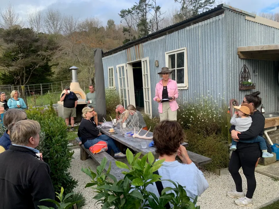 Volunteers and families sharing food at a picnic table outside a shed